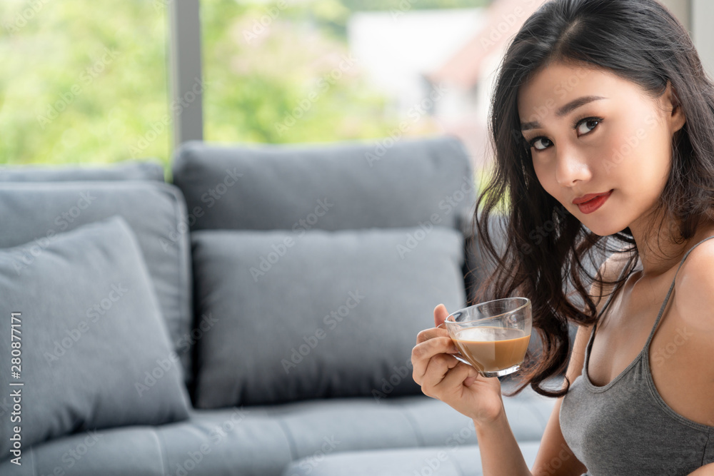 亚洲年轻女子早上坐在沙发上喝咖啡。