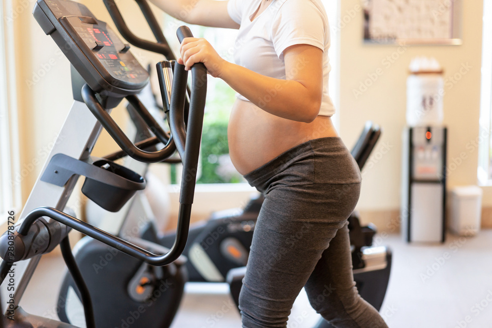 Active pregnant woman exercise in fitness center at yoga room. The young expecting mother holding ba