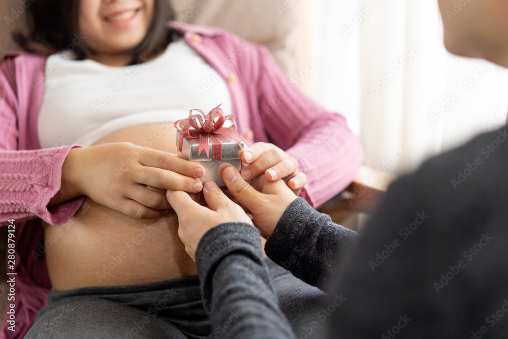 Pregnant couple of husband and wife feels love and relax at home. Young expecting woman holds baby i