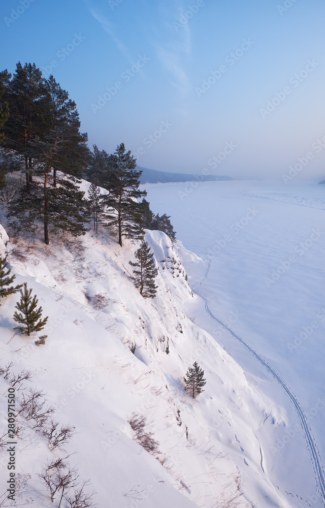 Steep slope of river Tom under the snow and ice in winter season