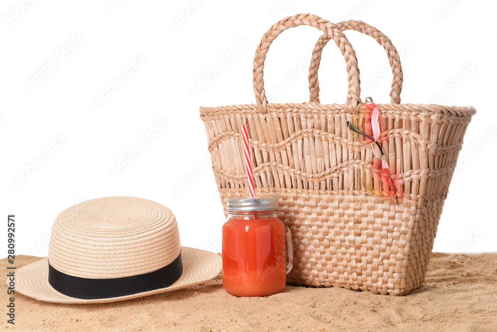 Beach bag and accessories on sand against white background