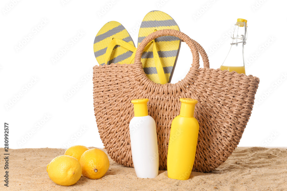 Beach bag, cosmetics and lemons on sand against white background