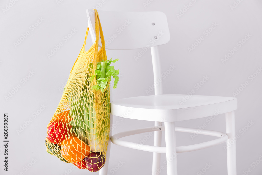 Mesh eco bag with products hanging on chair against light background