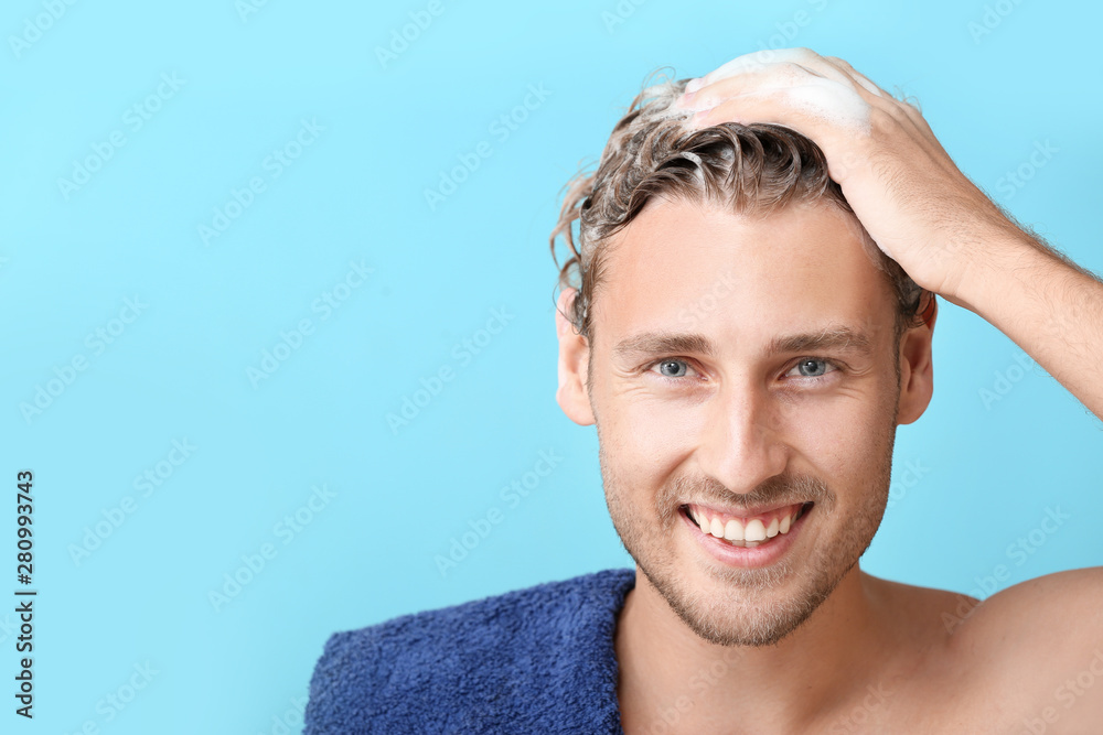 Handsome young man washing hair against color background