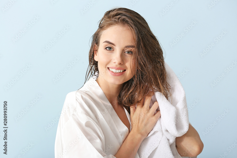 Beautiful young woman wiping hair after washing against color background