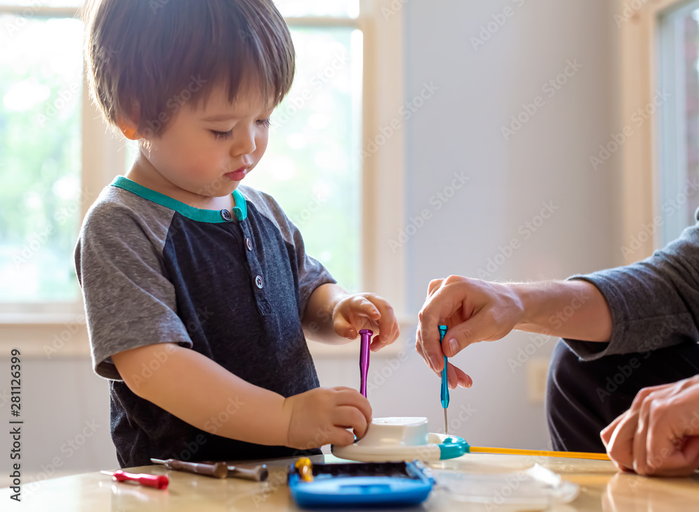 蹒跚学步的男孩玩工具并帮助修理他的玩具