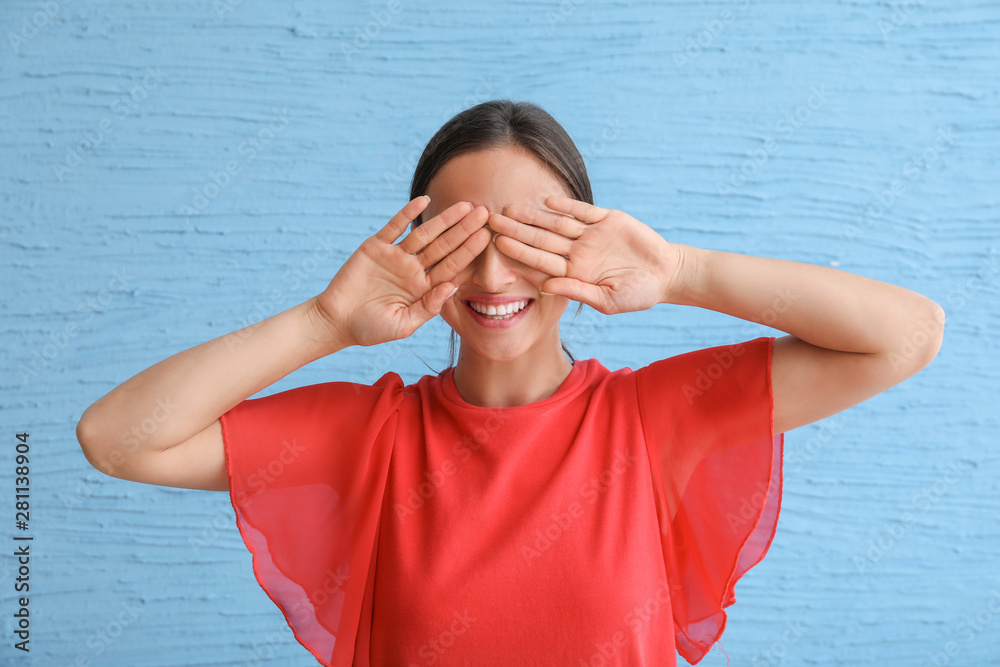 Young woman covering her eyes on color background