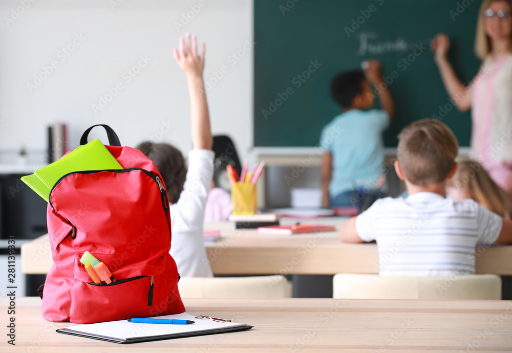 School backpack with stationery on table in classroom