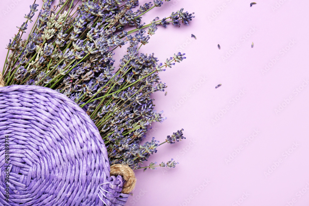 Beautiful lavender flowers with wicker bag on color background