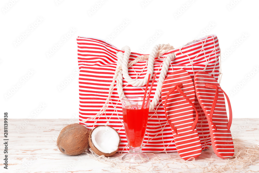 Beach bag, cocktail and accessories on table against white background