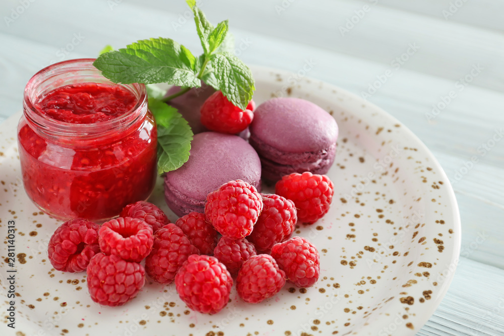 Plate with fresh raspberries, jam and macarons on white wooden table