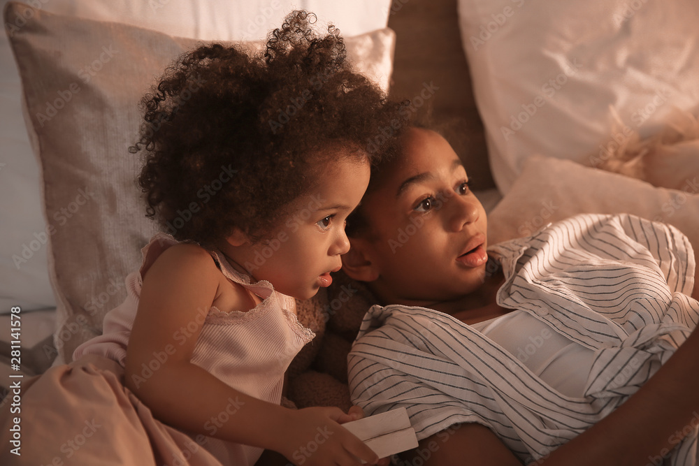 Cute African-American sisters watching cartoons in bedroom