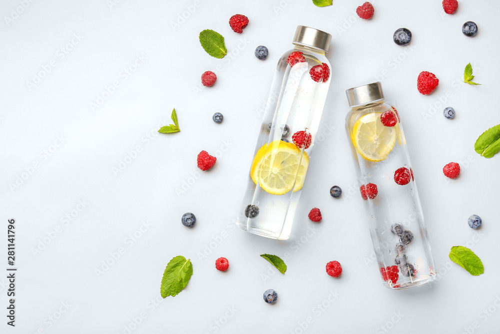 Bottles of tasty infused water on light background