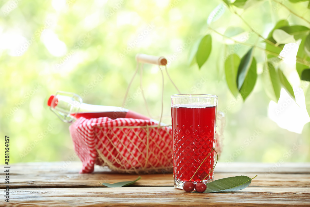 Glass of tasty cherry juice on wooden table outdoors