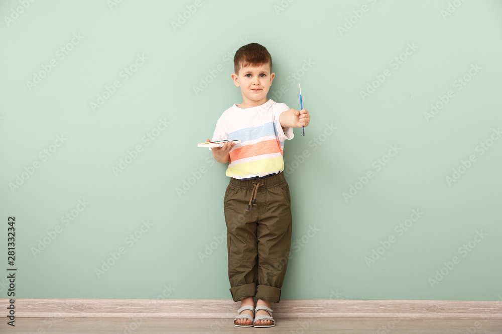 Cute little boy with paints and brush near color wall