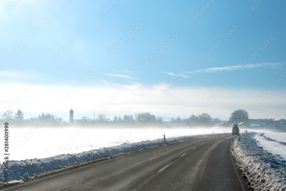 Landstraße in ländlicher Gegend, verschneite Winterlandschaft mit Morgennebel