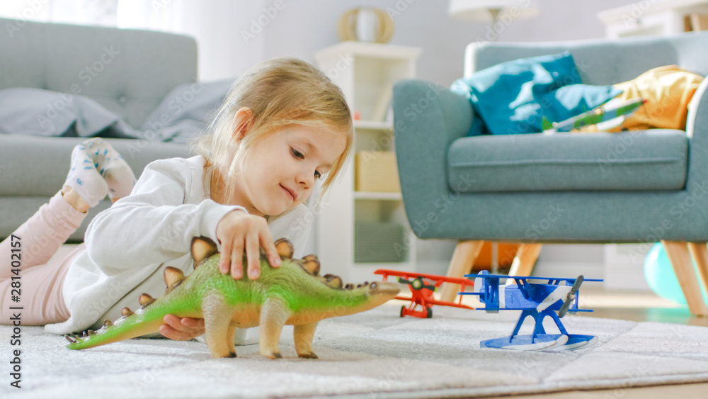 Cute Little Girl Blond Laying on a Carpet at Home, Plays with Toy Dinosaurs and Airplanes. Happy Chi