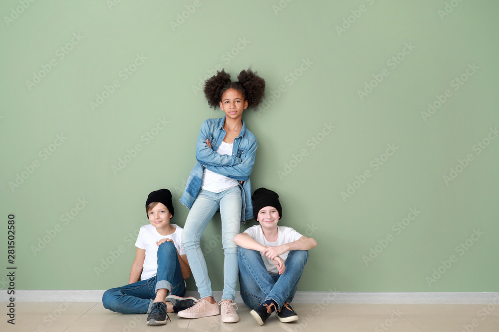 Stylish children in jeans clothes near color wall