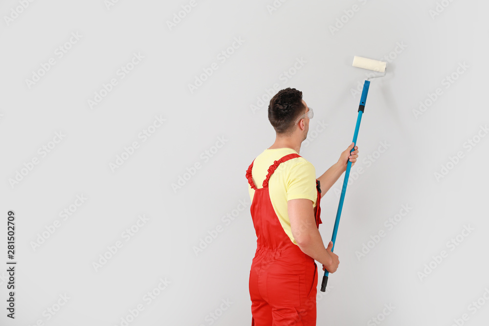 Male decorator painting light wall