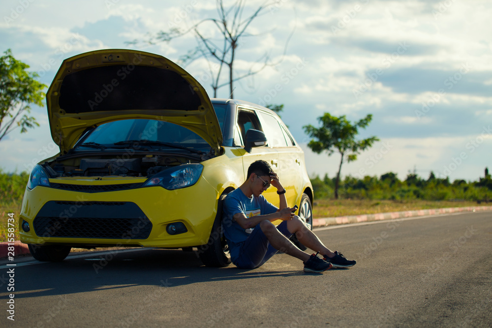 Stressed man sitting after a car breakdown at the countryside of the road and hand hold mobile phone