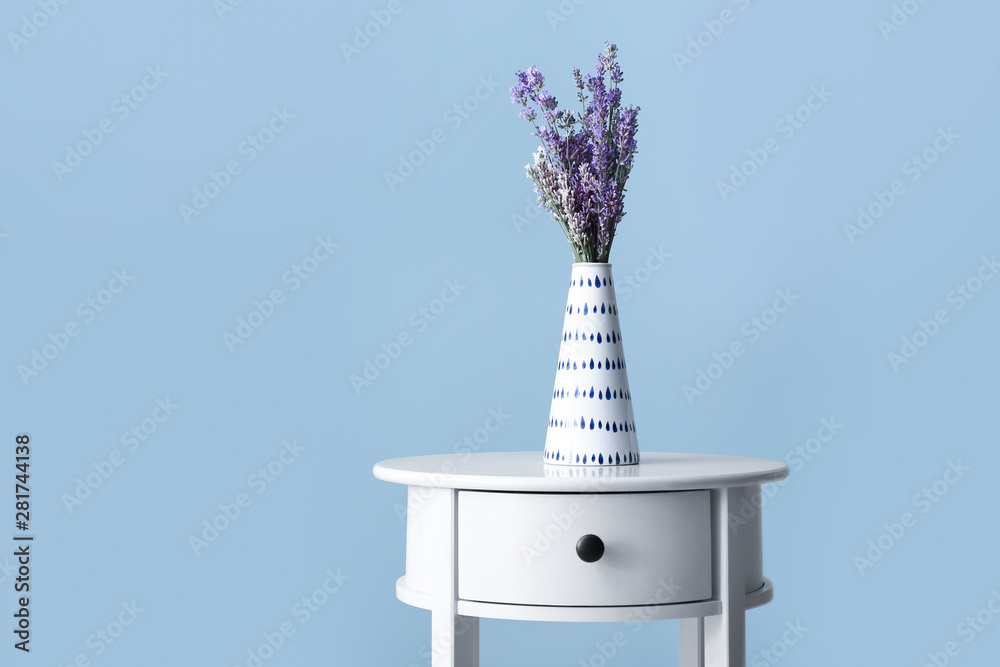 Beautiful lavender flowers in vase on table against color background