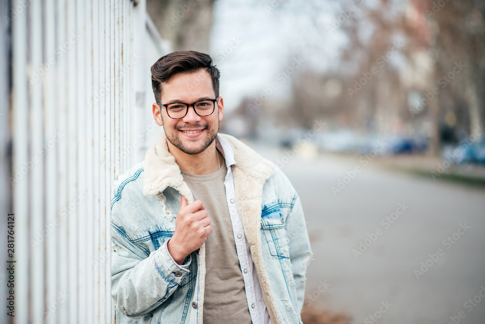 Portrait of a trendy young man at the city street, smiling at camera.