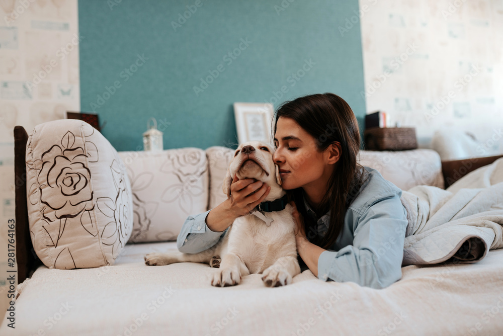 Young woman kissing labrador puppy in bed.