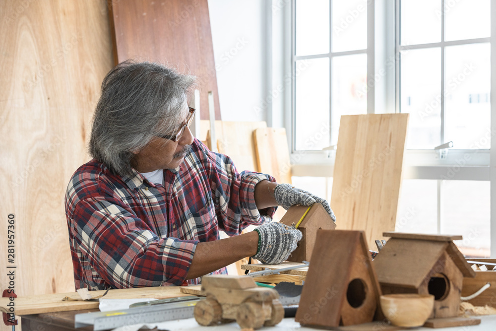 Asian man carpenter working on woodworking table in home carpentry shop, Old asian man works in home