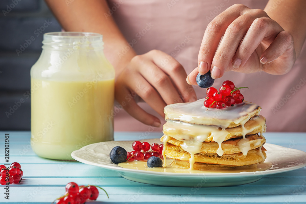 A girl in a pink apron decorates pancakes with blueberries and red currants. Tasty pancakes with con