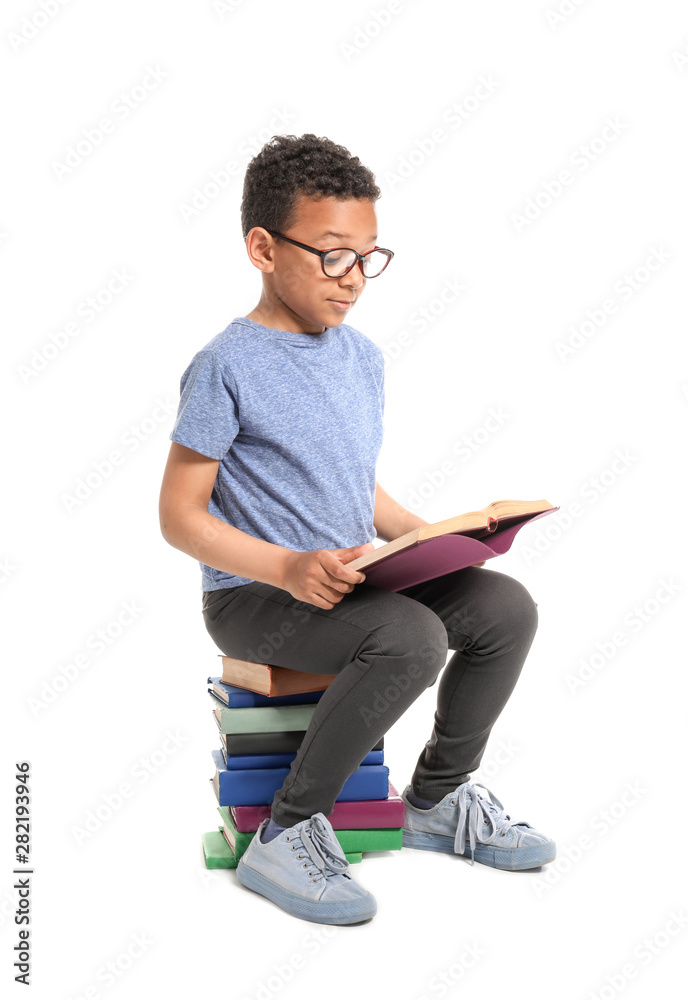 Cute African-American boy reading books on white background