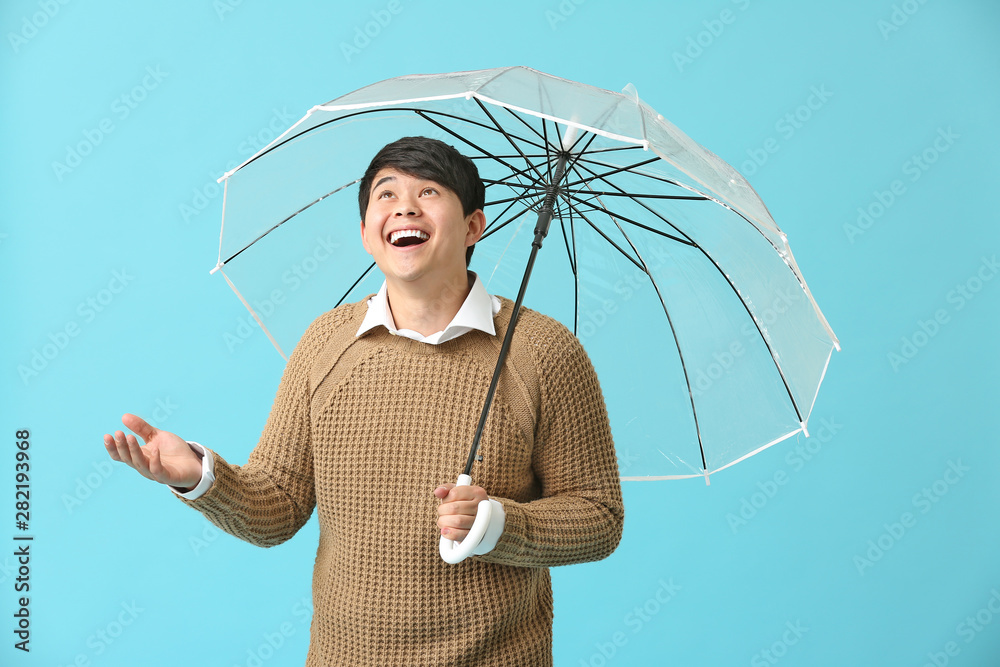 Handsome Asian man with umbrella on color background