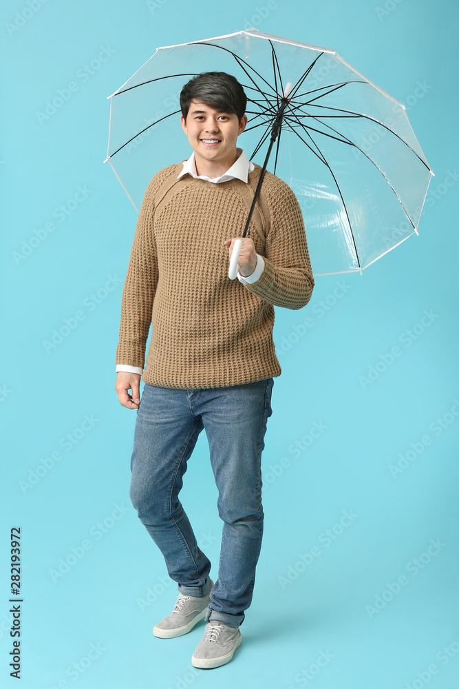 Handsome Asian man with umbrella on color background