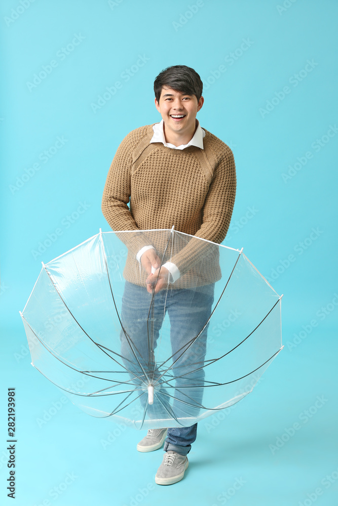 Handsome Asian man with umbrella on color background