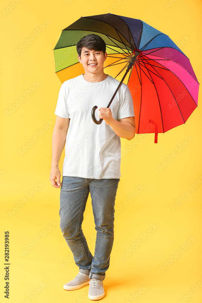 Handsome Asian man with umbrella on color background