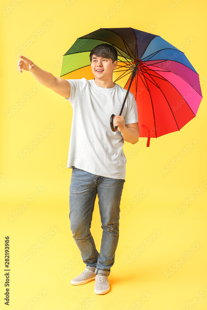 Handsome Asian man with umbrella on color background