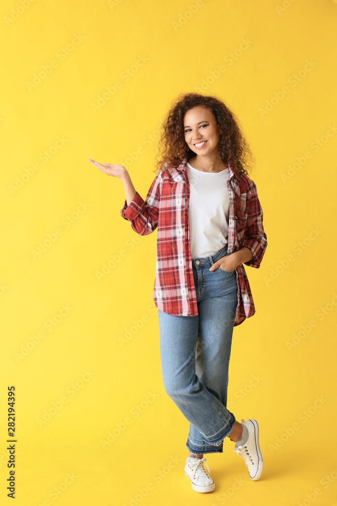 Beautiful African-American woman showing something on color background