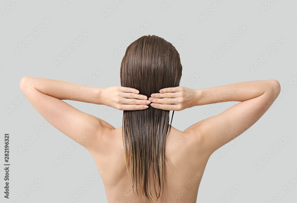 Beautiful young woman after washing hair against grey background, back view