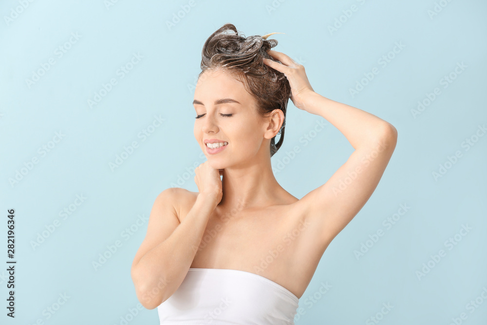 Beautiful young woman washing hair against color background