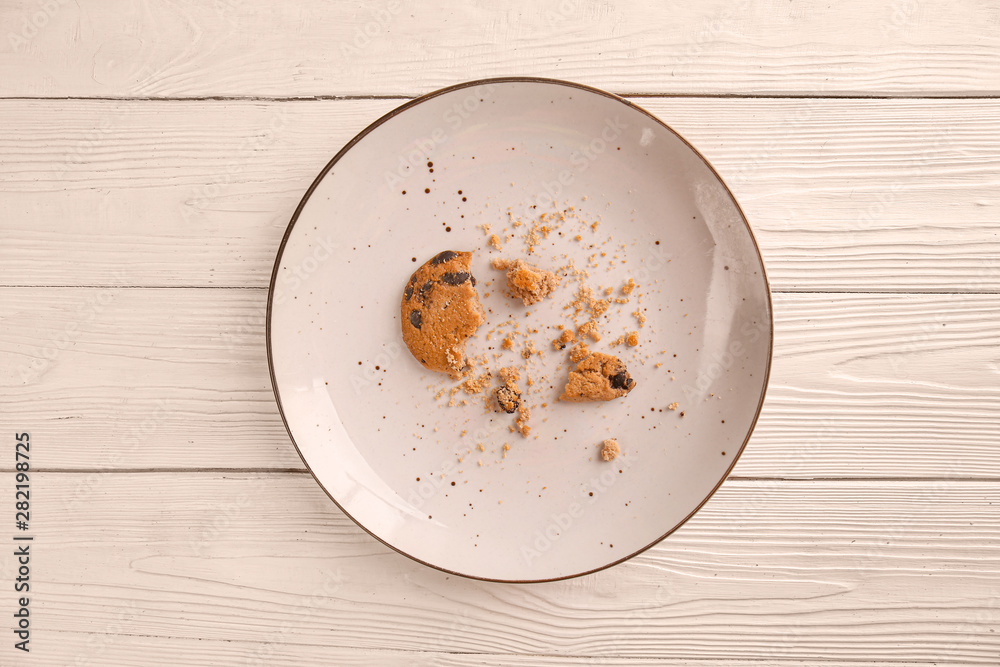 Plate with crushed cookie on light wooden background