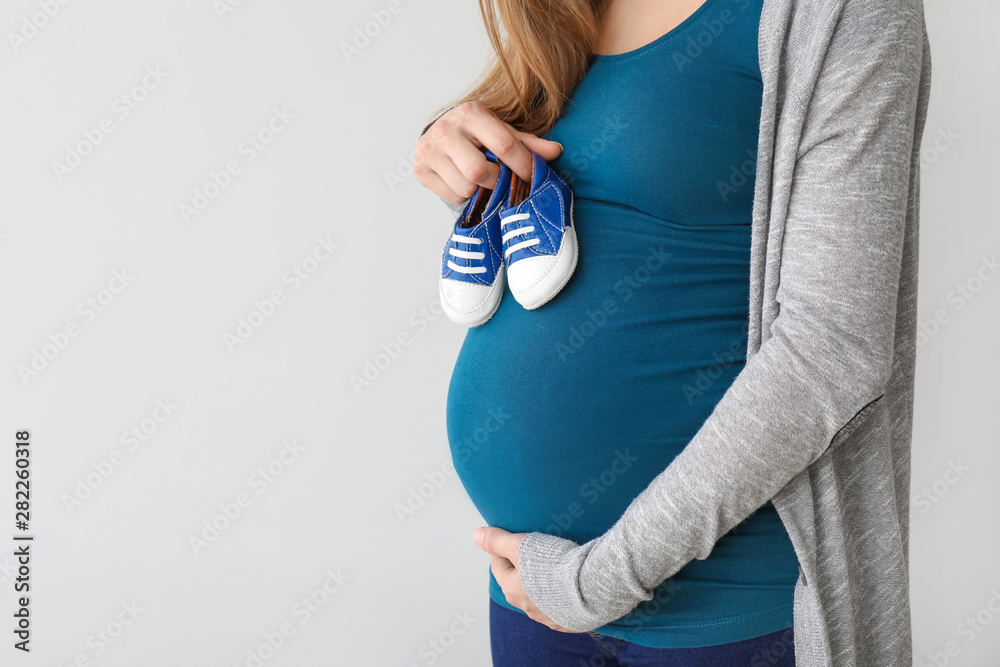 年轻孕妇穿着浅色背景的婴儿鞋