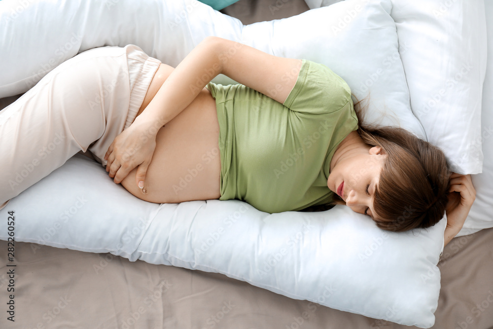 Young pregnant woman sleeping on maternity pillow at home