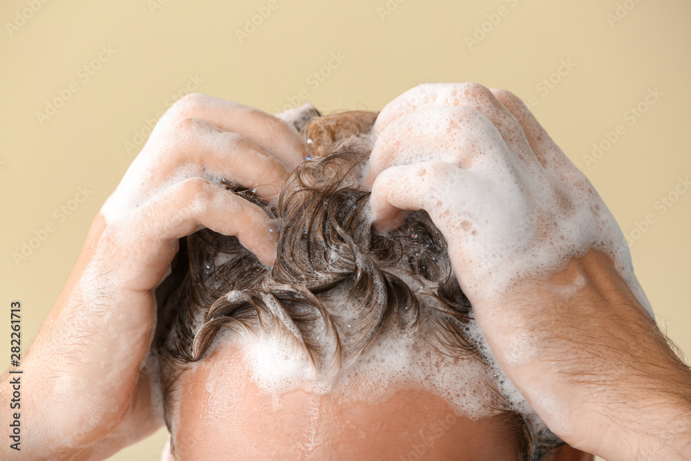 Handsome young man washing hair against color background, closeup