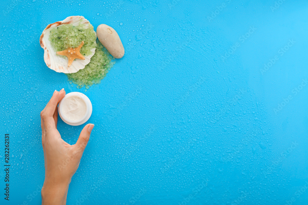 Female hand with natural cream and sea salt on color background