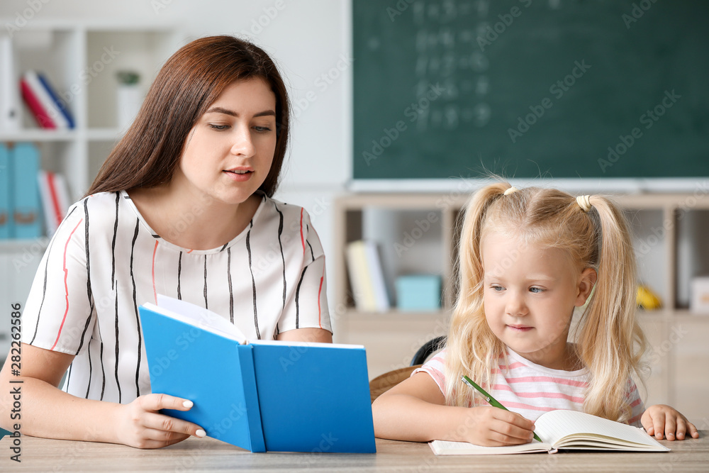 Teacher helping little girl to do task in classroom