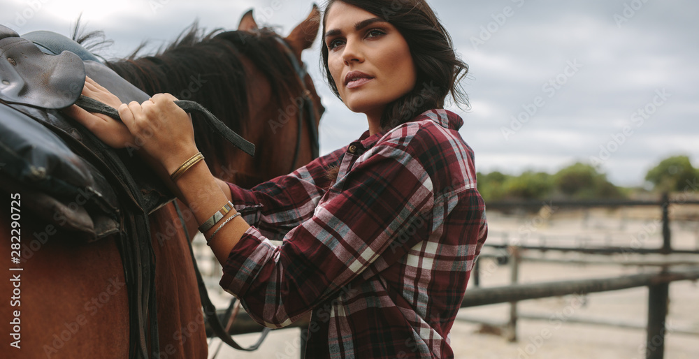 Cowgirl saddling a brown horse