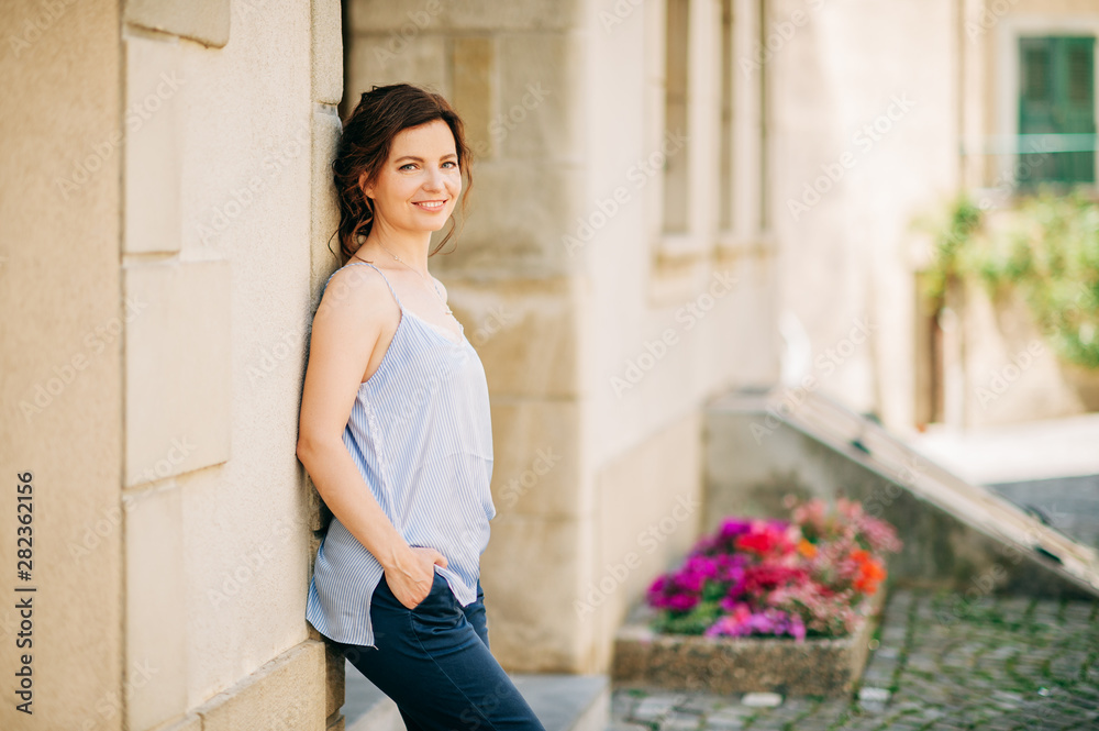 Outdoor portrait of beautiful young woman with dark hair, leaning on the wall