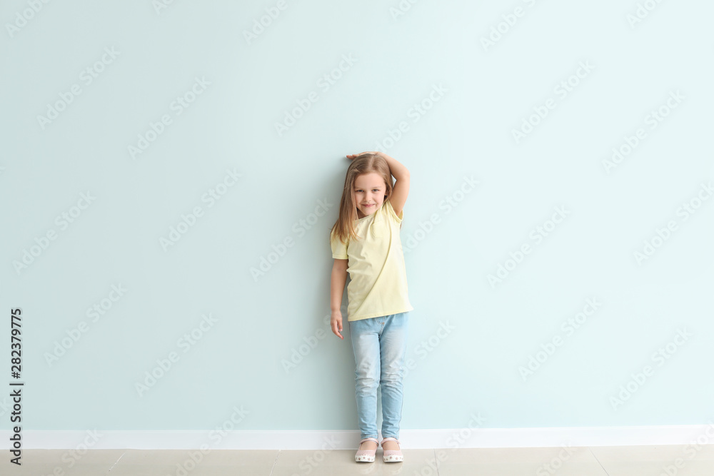 Cute little girl measuring her height near wall