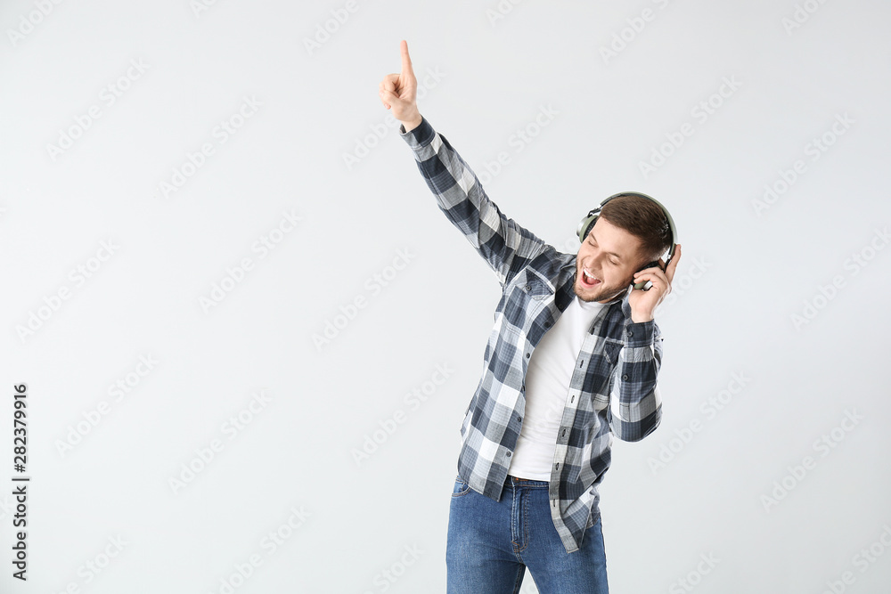 Handsome young man listening to music on light background