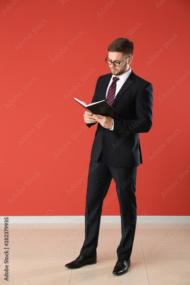 Handsome businessman with book near color wall