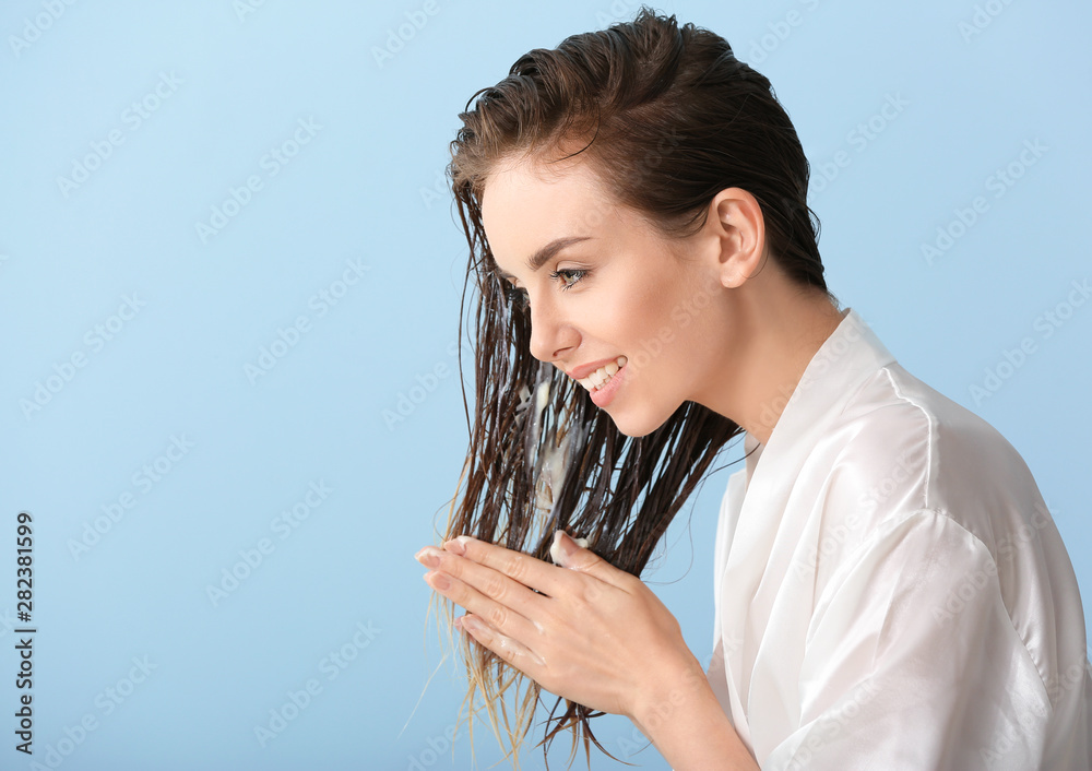 Beautiful young woman applying mousse on her hair after washing against color background